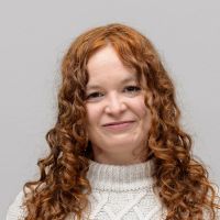 Anna Schneider - Assistente allo sviluppo commerciale: donna sorridente con lunghi riccioli rossi e occhi marroni.