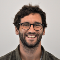 Markus Heigl - Developer: Smiling man with black, medium-length beard; black, wavy hair and black, roundish, thick glasses.