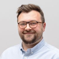 Ben Sandler – Sales Manager: Lächelnder Mann mit dunkelbraunen Haaren, dunklem Bart und eckiger Hornbrille