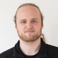 Sebastian Grzesny - Senior Developer: Hombre con pelo largo, rubio y ondulado recogido en una trenza; barba clara de longitud media y ojos azules.