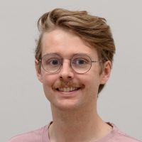 Charles Bailey - UI/UX Designer : homme souriant à la moustache rouge ; cheveux roux ondulés et fines lunettes rondes gris-argent.