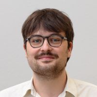 Severin Simmler - Senior Data Scientist : homme souriant aux cheveux brun foncé ; barbe courte et noire ; lunettes noires, épaisses et carrées.